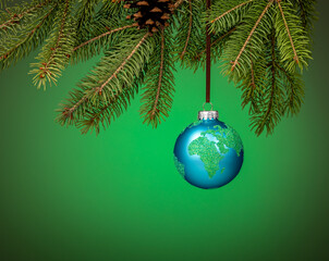 Globe christmas ornament hanging from a tree branch on green.