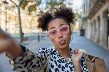 Adorable teenage girl with two combed buns keeps lips rounded stretches arm and makes selfie...