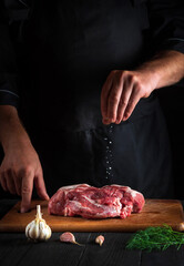 The cook sprinkles the meat with salt. Preparing meat before baking. Working environment in the kitchen of a restaurant