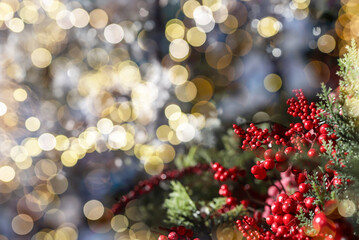 Fototapeta na wymiar Christmas background with blurred bokeh of Xmas glowing lights and fir tree branch with red berries. Copy space for text.