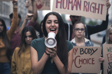 Group of young people protesting on the street with signs raised to promote women rights and right...