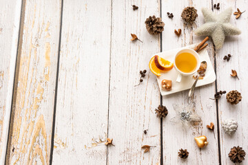 Christmas background with a warming cup of tea and natural decoration like pine cones, nuts, and a star on a light, rustic wooden background in vintage style