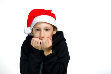 a boy in a red Santa hat holds his hands in front of his face