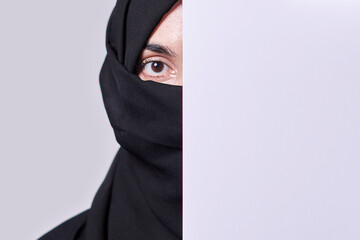 Young muslim women with expressive eyes covering part of her face with white paper. Muslim girl in...