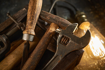 Wooden tool box of used hand tools with old and dirty, rusty wrenches, hammers, and old light bulb