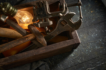 Wooden tool box of used hand tools with old and dirty, rusty wrenches, hammers, and old light bulb
