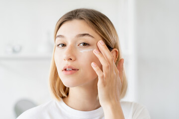 Under eye cream. Skincare moisturizing. Morning treatment. Pretty young woman applying beauty...