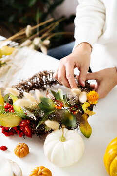 Woman hands with diy floral autumn wreath with driad grass, plant and berry