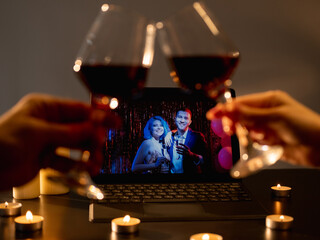 Anniversary party. Home meeting. Virtual greeting. Defocused cheering two glass of wine on friendly congrats on laptop background in festive candles decorated room interior.