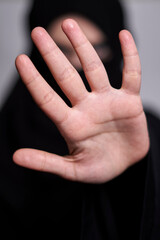 A Muslim woman in traditional black clothing nikab showing stop hand gesture. Role of women in...