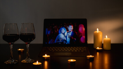 Anniversary party. Online greeting. Virtual friends. Two glasses of wine on festive candles light decorated table with laptop male female couple congrats dark home interior.