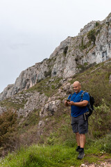 Naklejka na ściany i meble Selective focus on a muscular Caucasian man and hiker in the mountains, using the smartphone.