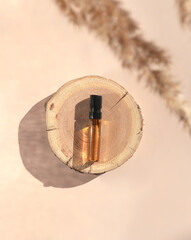 Glass perfume sample with brown liquid on a wooden tray lying on a beige background with pampas grass. Luxury and natural cosmetics presentation. Tester on a woodcut in the sunlight. Top view