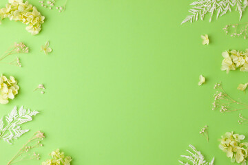 Fototapeta na wymiar Cosmetic background with flowers on green. Flat lay, copy space