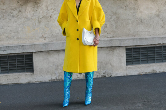 Milan, Italy - September 24, 2021: Street style outfit, fashionable woman wearing a yellow oversized long coat, a white Cleo shoulder bag from Prada, blue shiny boots in Milan, Italy.