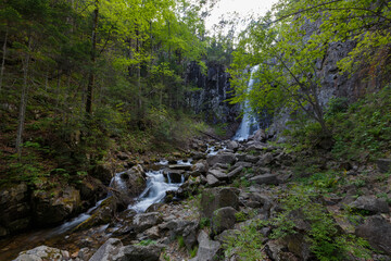 The nature of the Far East and the Primorsky region of Russia. Picturesque waterfall in the evening. Water flows down a natural waterfall in a dense summer forest.