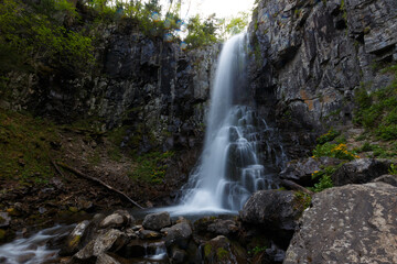 Fototapeta premium The nature of the Far East and the Primorsky region of Russia. Picturesque waterfall in the evening. Water flows down a natural waterfall in a dense summer forest.