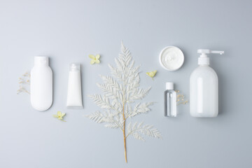 Cosmetic composition with cosmetic skin care products and flowers on grey background. Flat lay, copy space