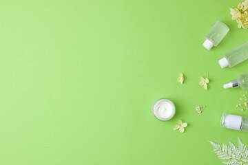 Cosmetic skin care products with with flowers on green background. Flat lay, copy space