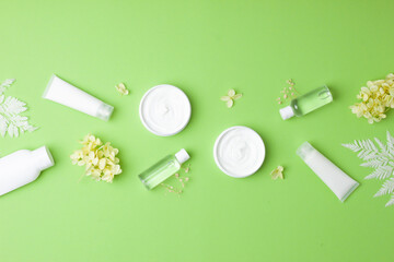 Cosmetic skin care products with with flowers on green background. Flat lay, copy space