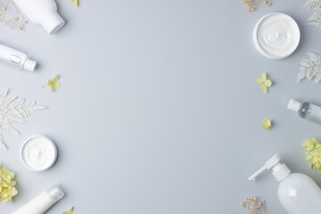 Cosmetic skin care products with with flowers on grey background. Flat lay, copy space