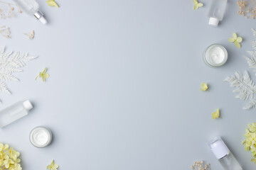 Cosmetic skin care products with with flowers on grey background. Flat lay, copy space