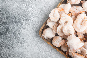 Frozen peeled boiled shrimps, on wooden tray, on gray background, top view flat lay, with copy space for text