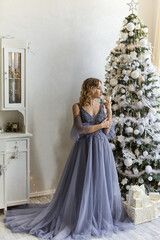 Fototapeta premium Beautiful young woman in the evening dress stands in a room decorated for Christmas