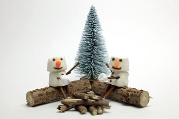 marshmallow snowmen with happy faces sitting on logs toasting marshmallows.