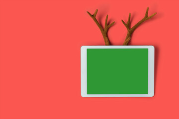 White touchpad with blank touchscreen with fake toy antlers of a deer on a red background. Merry Christmas or Happy New Year concept with space for your copy