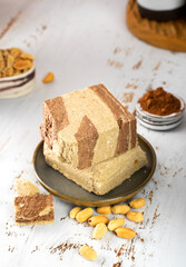 Minimalistic. Tasty eastern sweet dessert halva from sunflower seeds, cashew, cocoa and tahini on beige wooden background.Traditional dessert confection in Middle East, Balkans and west Asia.Vertical.