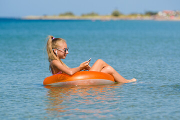 Teenage girl swims in the sea on a circle with a phone