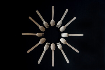 Wooden disposable spoons and forks made from birch tree lies on black background. Round frame (looks like a clock) from biodegradable cutlery. Copy space for your text. Environmental protection theme.