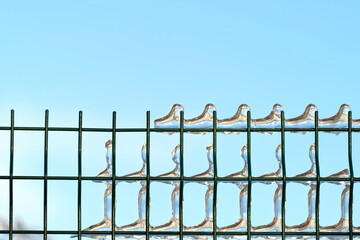Metal green lattice with ice on a blue sky background