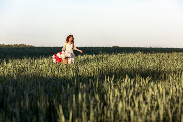 a red-haired girl in a dress walks through a field with a basket full of flowers