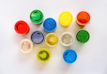 Color glitter paints in jars on a white background. Top view.