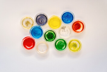 Color glitter paints in open  jars on a white background. Top view.