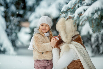 Cute little girl and mother are playing at snowy winter day in the park. Looking at the hands.