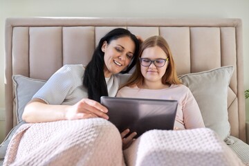 Mother and teenage daughter are resting at home together, use a digital tablet