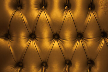 The texture of the leather sofa upholstery in gold color, with rivets.