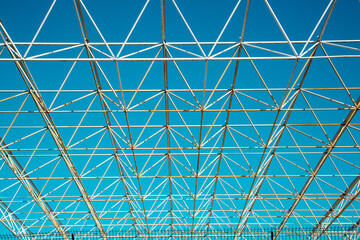 Obraz premium Openwork metal construction on a blue sky background on a clear sunny day, texture backgrounds for graphic design. Abstract wallpaper.