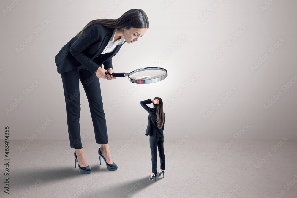 Poster Businesswoman in suit using magnifier magnifying glass to look at tiny subordinate on concrete background with shadow and mock up place. Hiring and dominance concept.