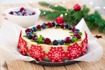 Festive cake for Christmas holidays. Recipe of cheesecake with blueberry and cranberry in pastry snowflakes with fir branches in Christmas lights. Original treats for winter holidays entertainment.