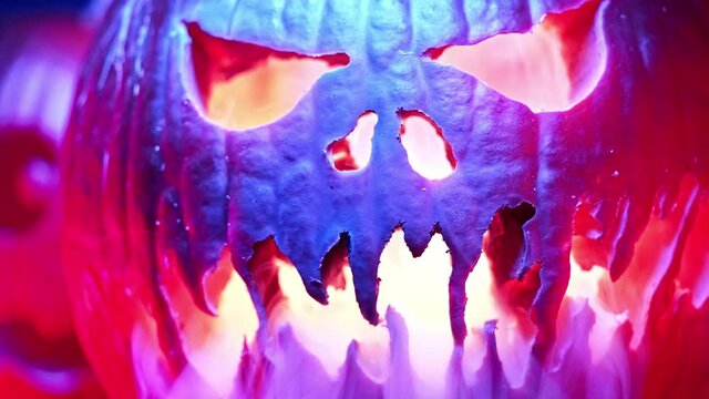 Scary carved halloween pumpkins with smoke under colorful neon light. Trick or treat background. Glowing face with flame inside. Symbol of All Hallows' Eve. Slow motion