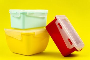 Multicolored plastic lunch boxes on yellow background, side view. Food containers of different shapes and sizes