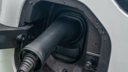 Close-up view of power supply plugged into an electric car being charged. White electric car charging.