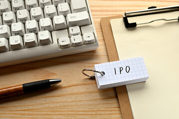 There is a word book with the word of IPO which is an abbreviation for initial public offering on the desk with a pen and a keyboard.
