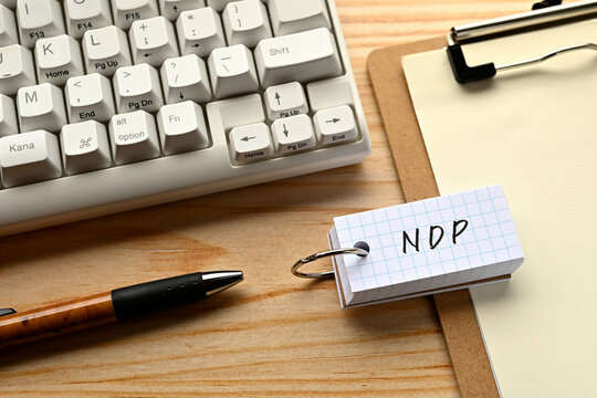 There is a word book with the word of NDP which is an abbreviation for net domestic product on the desk with a pen and a keyboard.