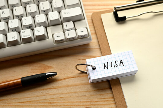 There is a word book with the word of NISA which is an abbreviation for Nippon Individual Savings Account on the desk with a pen and a keyboard.