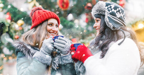Best friends enjoying mulled wine on Christmas market looking at camera